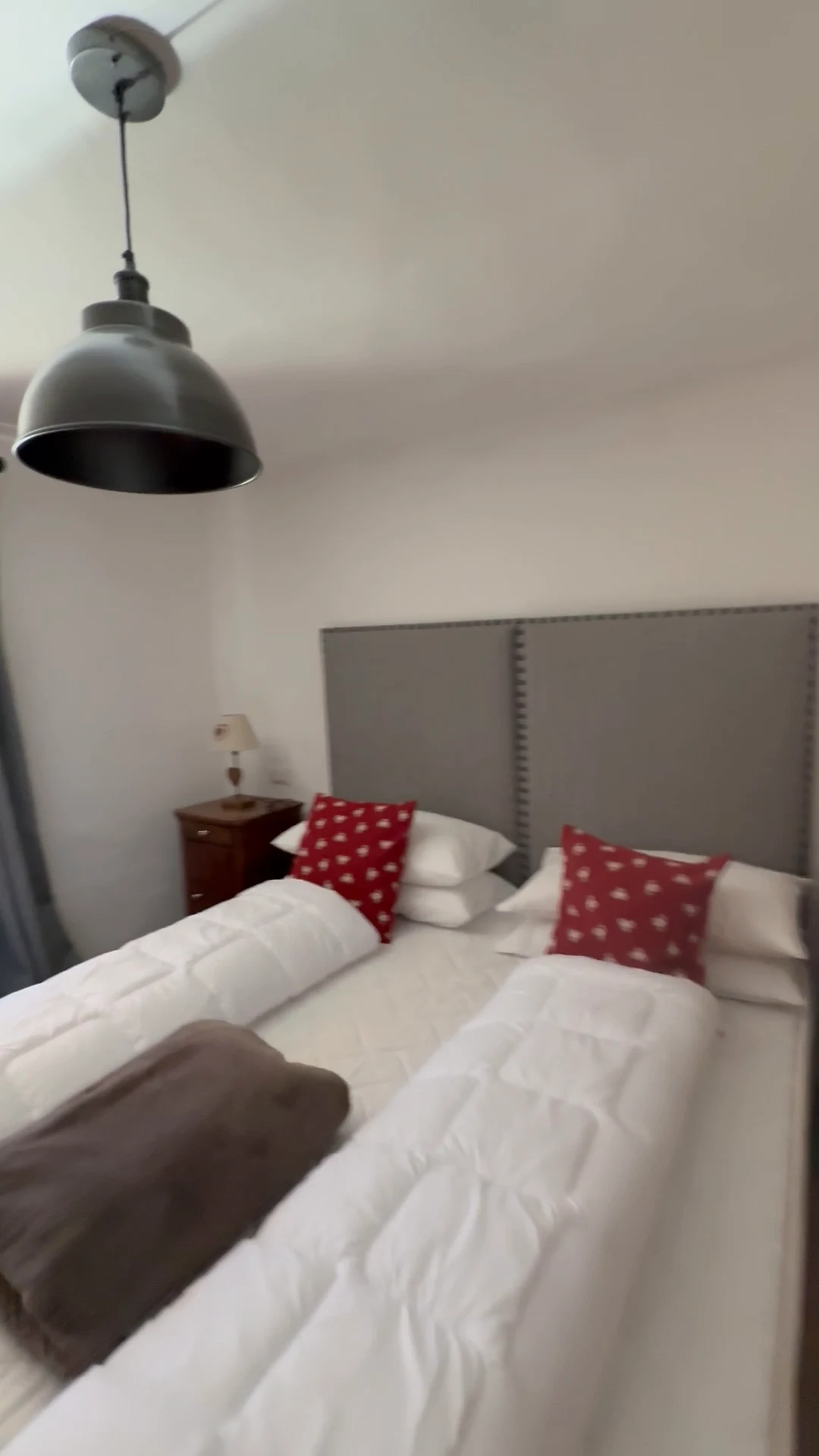 Cozy chalet bedroom with white bedding, red patterned cushions and a hanging pendant light