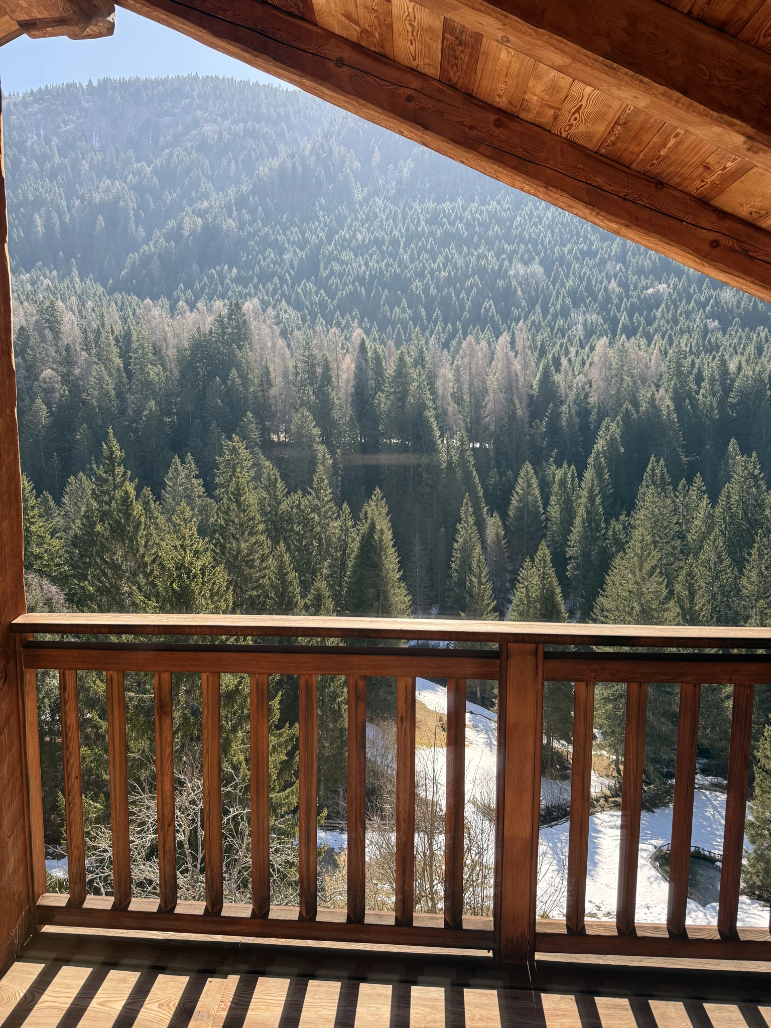 Snow-covered forested mountain view framed by a wooden chalet balcony